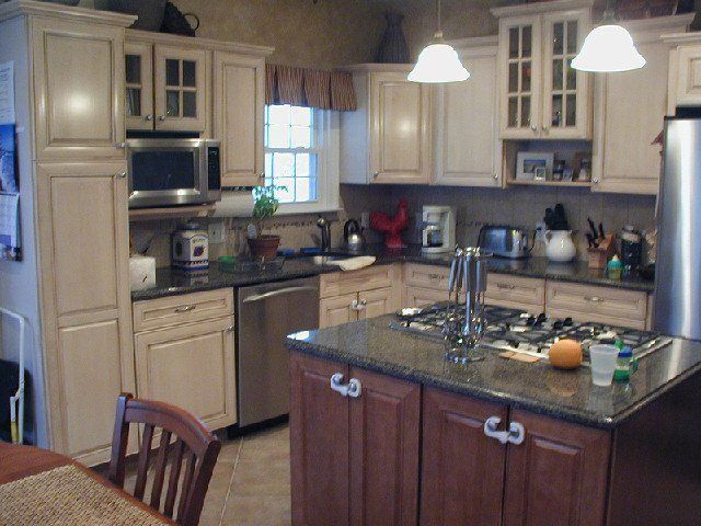 Bright kitchen with cream cabinets, granite island, hanging lights, and a window by the sink.