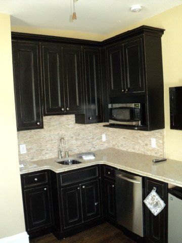 Small kitchen with black cabinets, stainless appliances, light countertop, and beige tile backsplash.