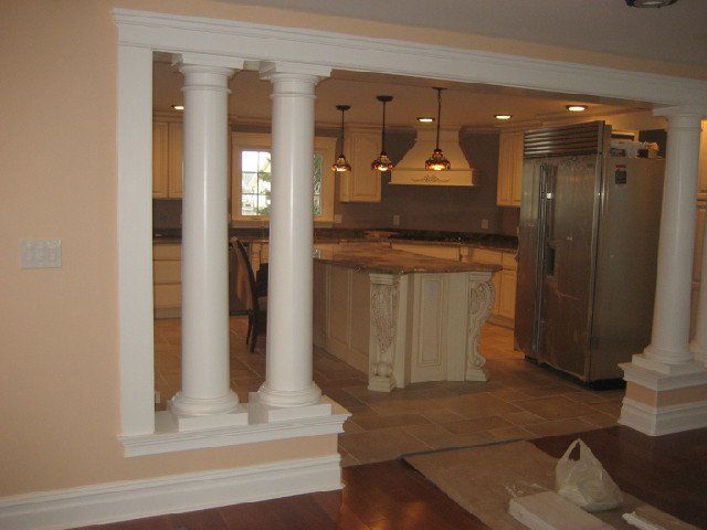 Open kitchen with white columns, granite island, and stainless steel refrigerator in a warm-toned home interior