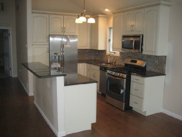 Modern kitchen with white cabinets, stainless steel appliances, dark granite counters, and wood floors