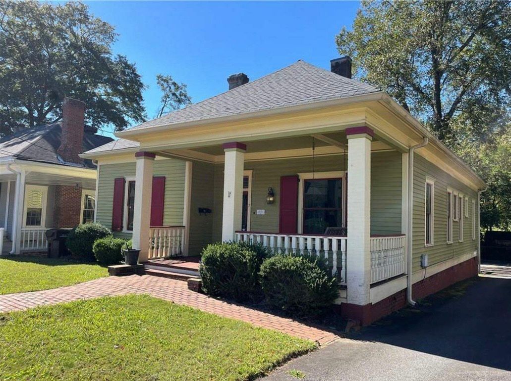 A small green house with a porch and a brick walkway.