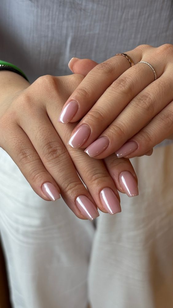 Close-up of two hands with glossy pale pink manicured nails and thin rings
