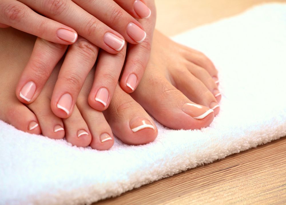 Two hands with pale pink manicured nails resting together on a white surface