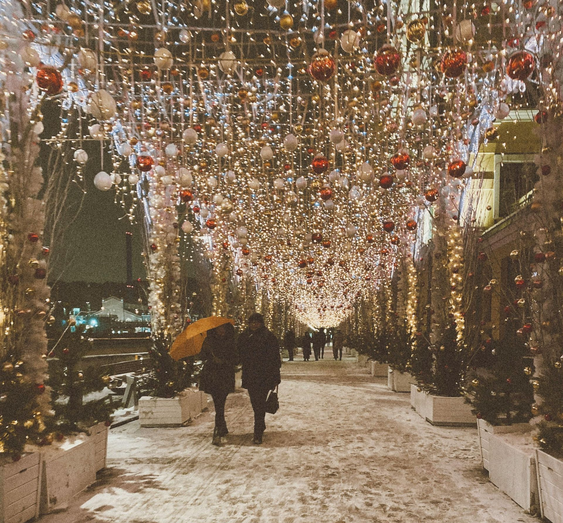 Couple walking under holiday lights & decorations on a snowy sidewalk. HunnyDo's Blog, Don't hibernate, Hunny