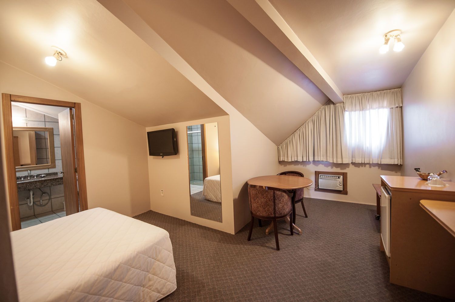 um quarto de hotel com cama, mesa, cadeiras e televisão.