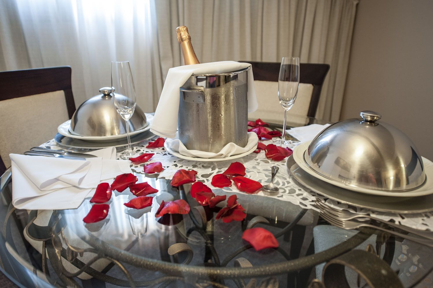uma mesa de vidro com uma garrafa de champanhe e pétalas de rosa