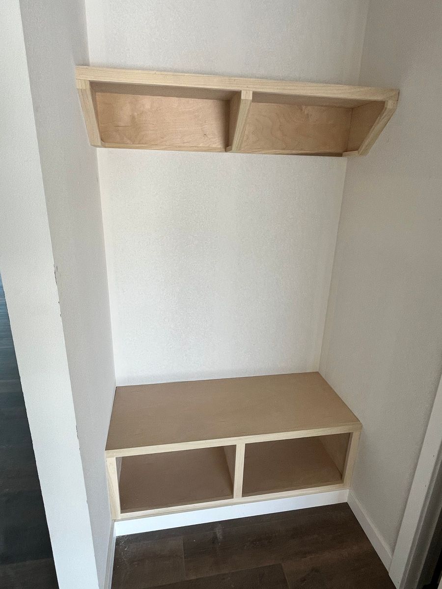 There is a bench and shelves in the corner of the room.