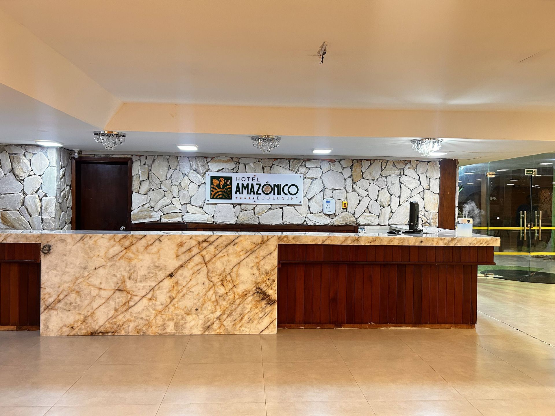 Balcão de recepção com bancada de mármore, parede de pedra ao fundo e logotipo do Hotel Amazonico.