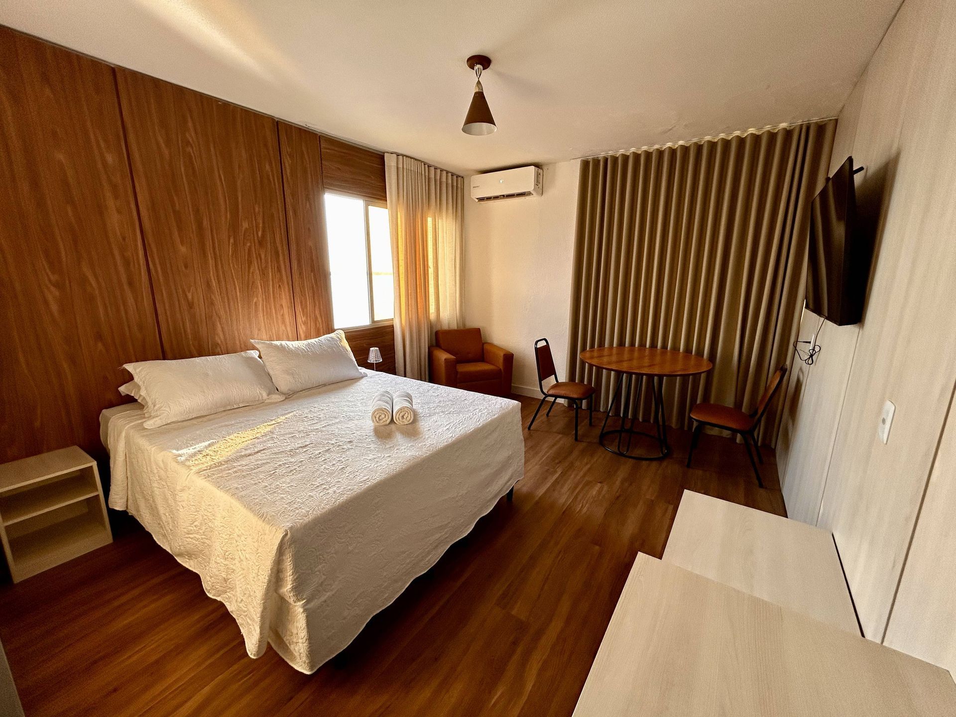 Quarto de hotel com paredes de madeira, uma cama, mesa, cadeiras e uma pequena área de estar.