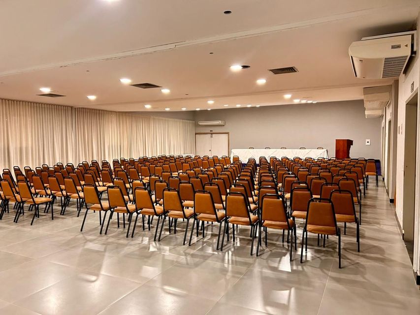 Sala de eventos vazia com fileiras de cadeiras voltadas para um palco com pódio.