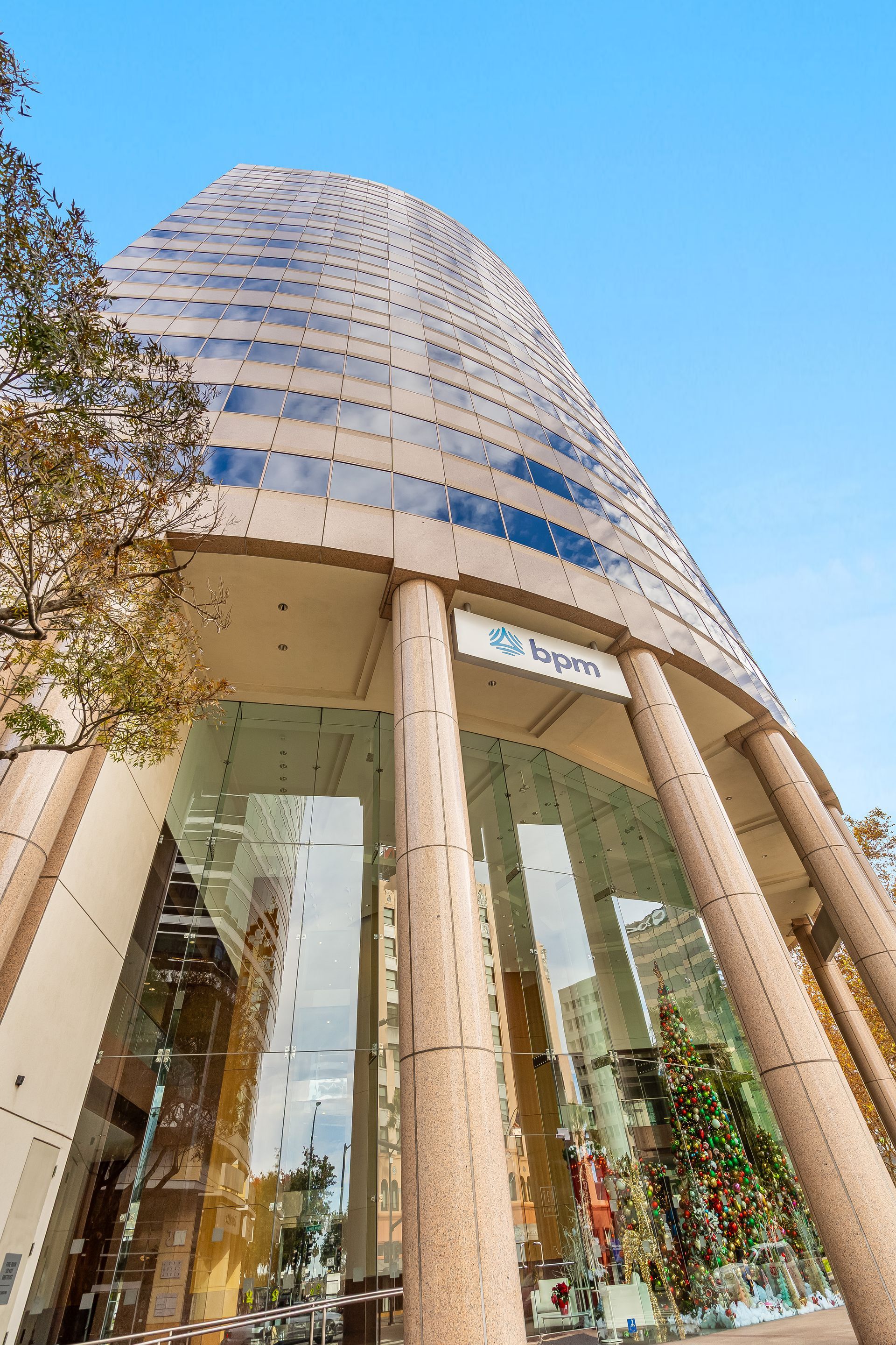 Tall glass and beige office building with rounded facade and large entry columns, blue sky.