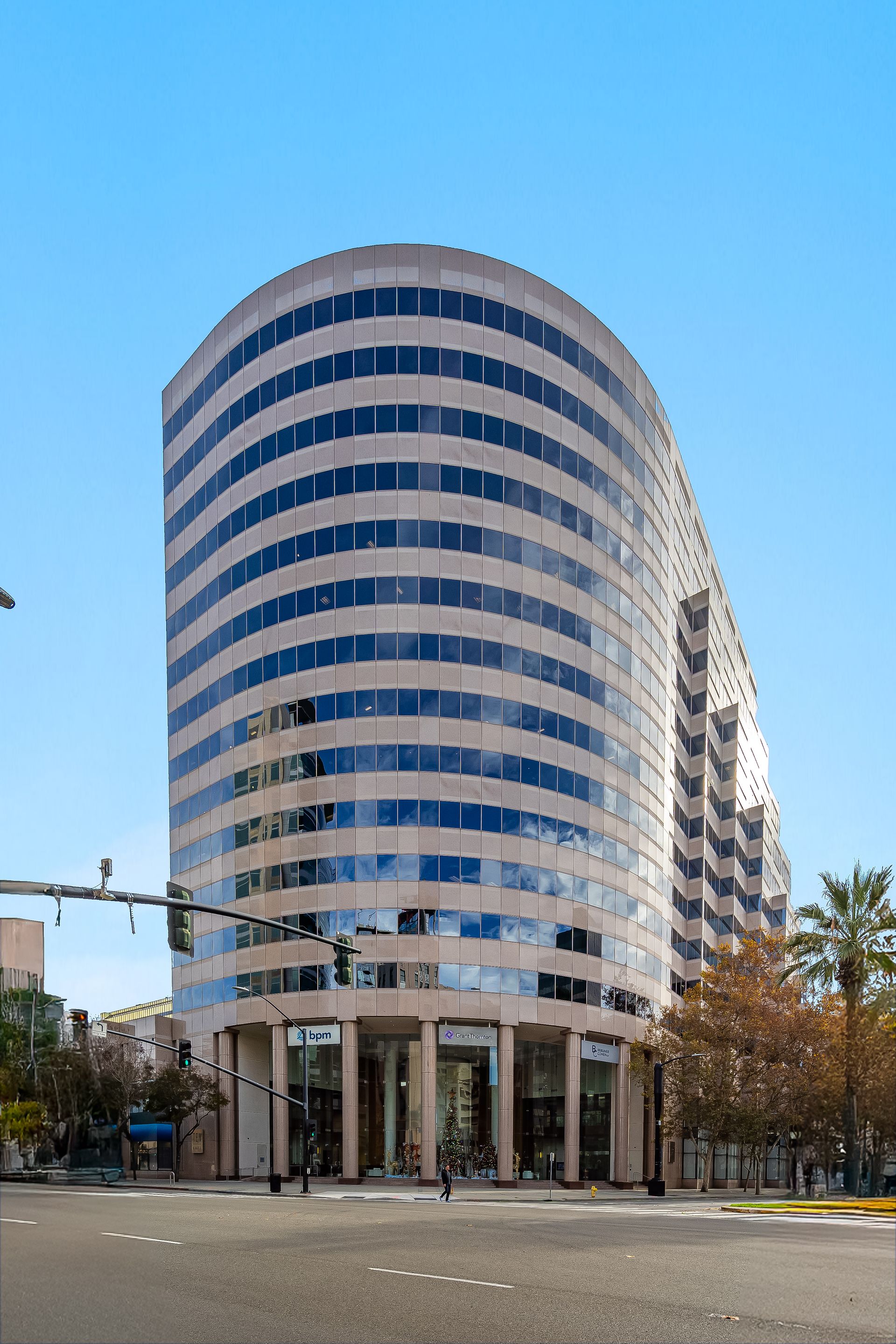 Curved, multistory office building with horizontal bands of windows under a blue sky.