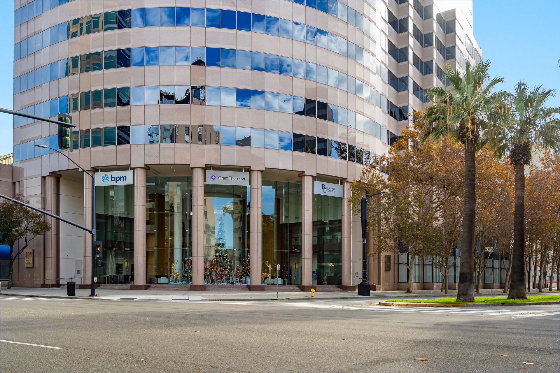 Exterior of a tall beige and glass office building with palm trees in front and a street.