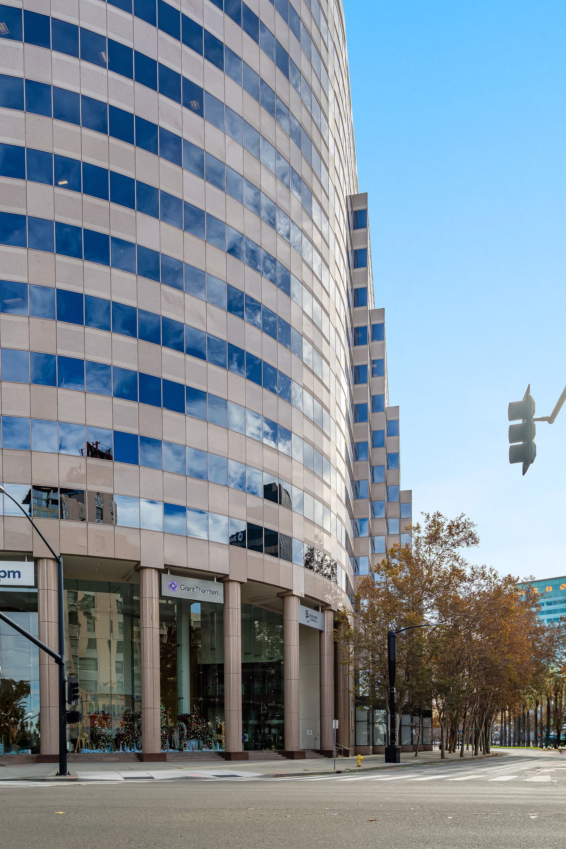 Curved beige and glass office building with street-level shops under a blue sky.