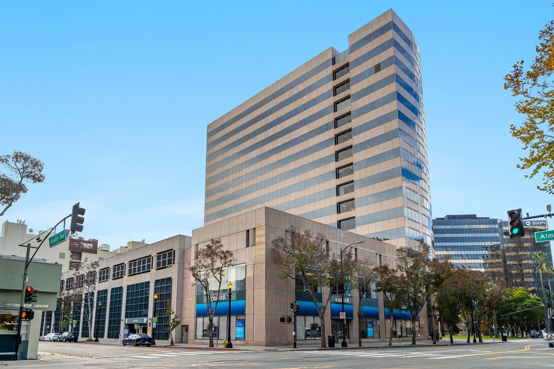 A tall, multi-story office building with a lower level, on a city street under a blue sky.