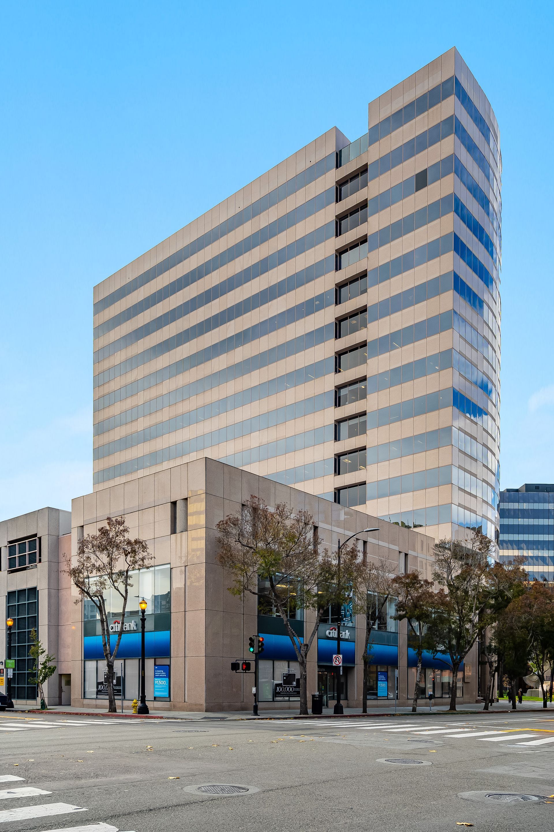 Office building with tan facade and blue-tinted windows above a two-story building on a city street.