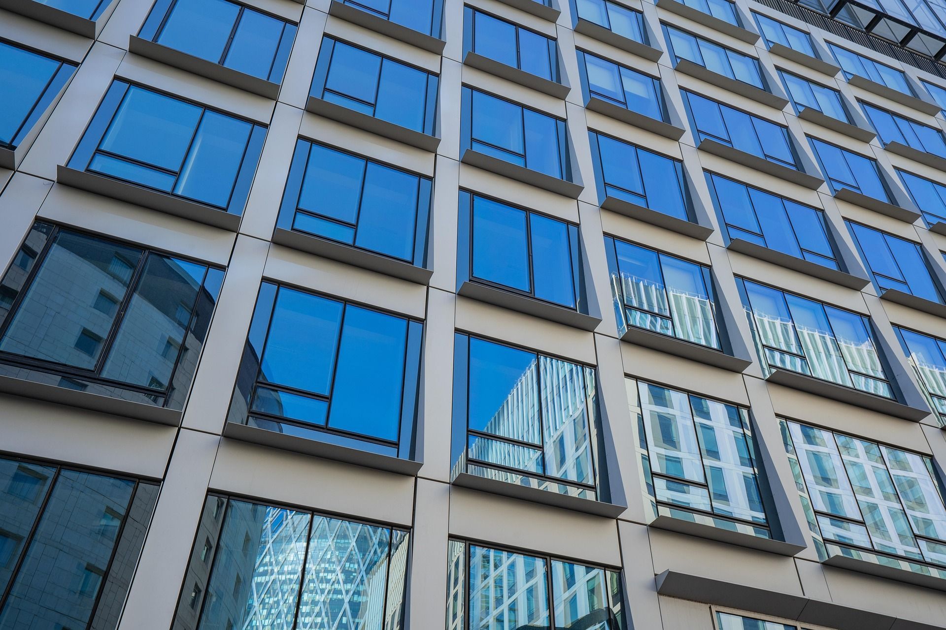Modern building exterior with many square, blue-tinted windows reflecting surrounding buildings.