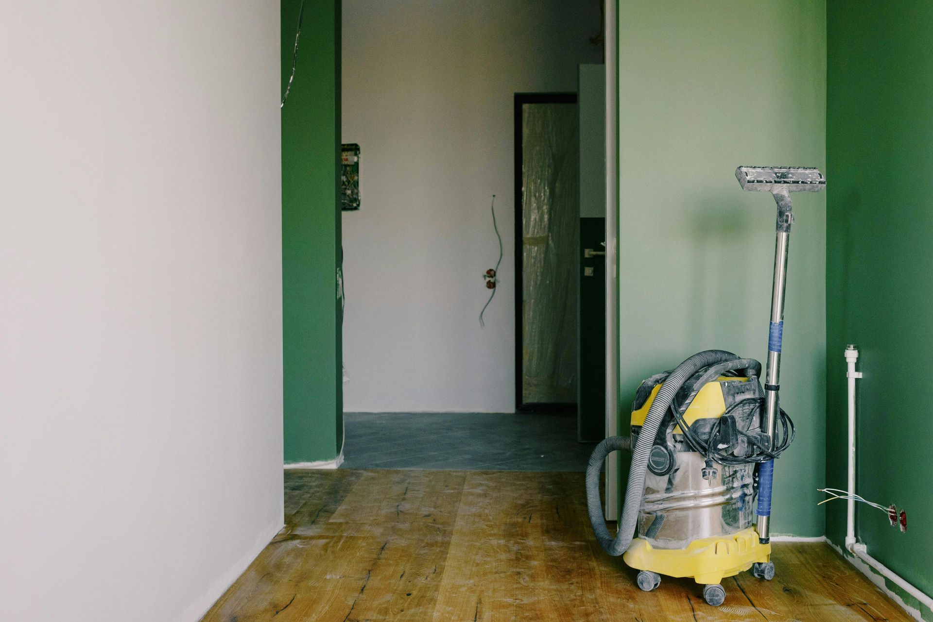 Room under renovation with a vacuum cleaner. Green and white painted walls, wooden floor.