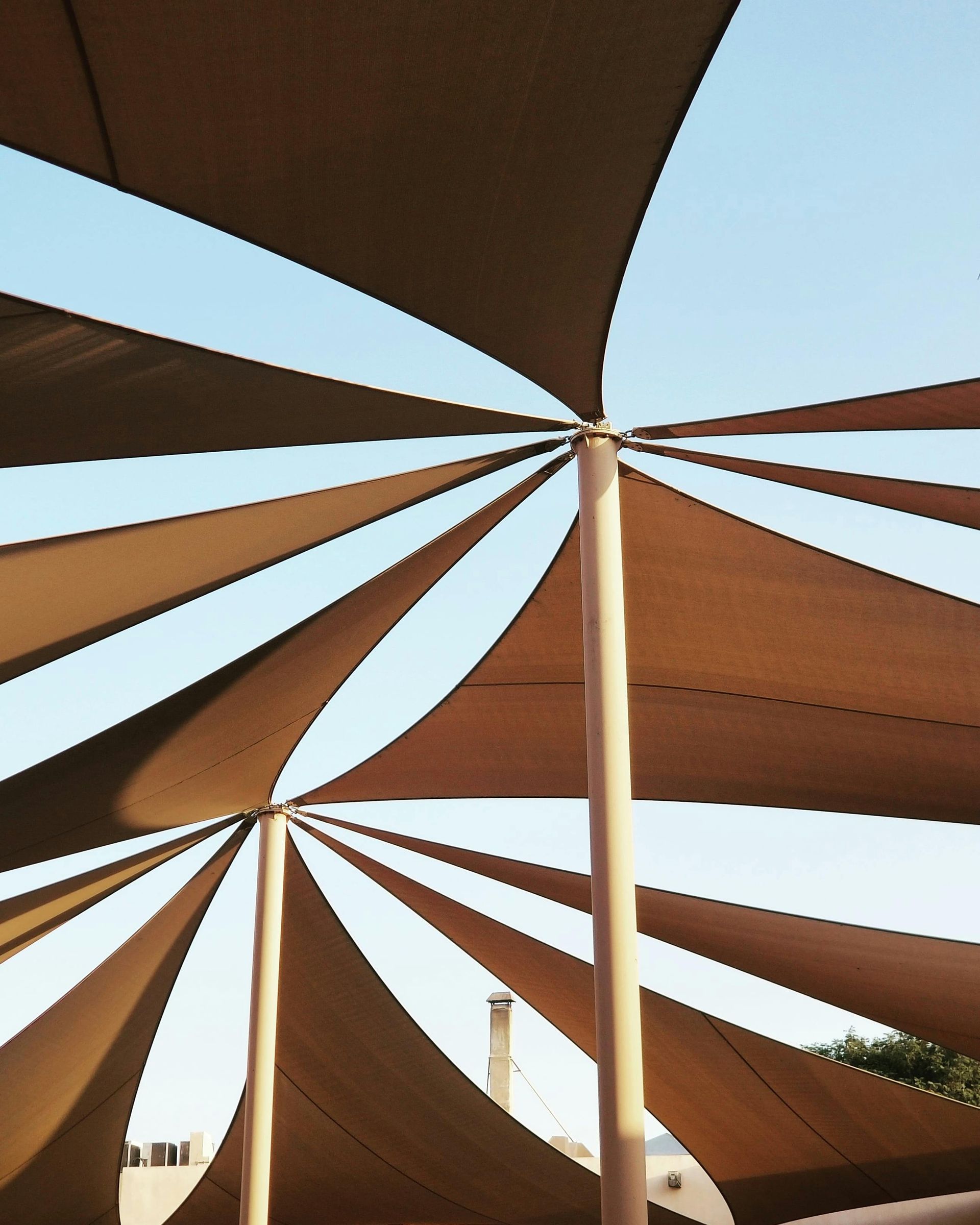 Beige shade sails stretch from wooden poles against a light blue sky.