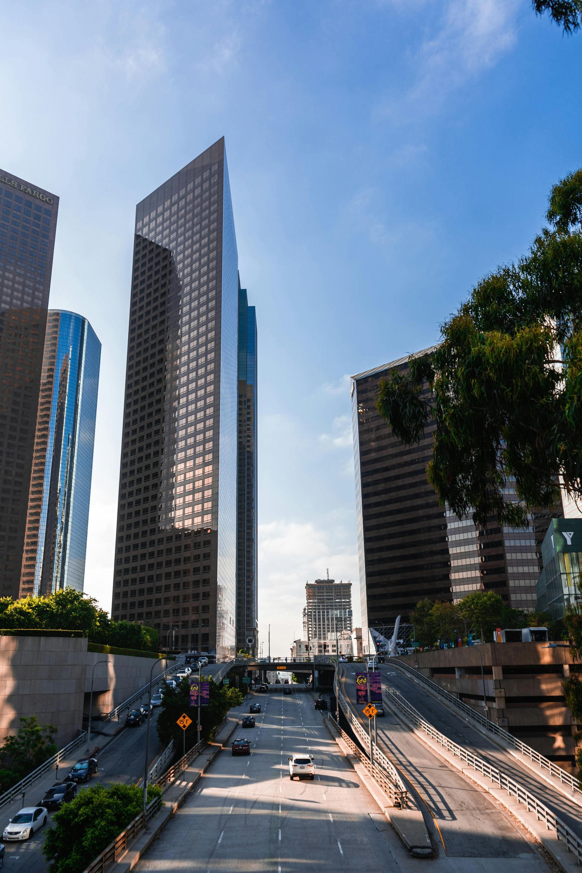Downtown Los Angeles cityscape with high-rise buildings and a multi-lane highway under a blue sky.