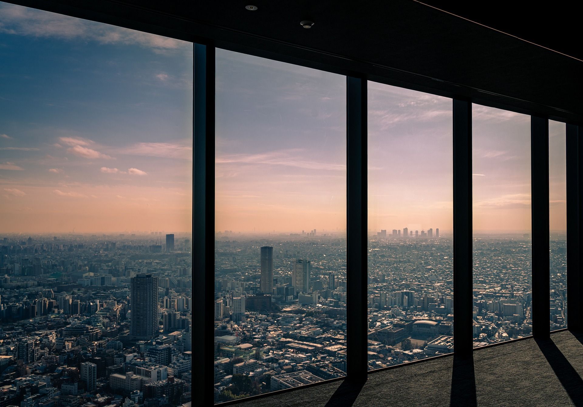 City skyline view through tall, dark framed windows at sunset; buildings, sky, light.