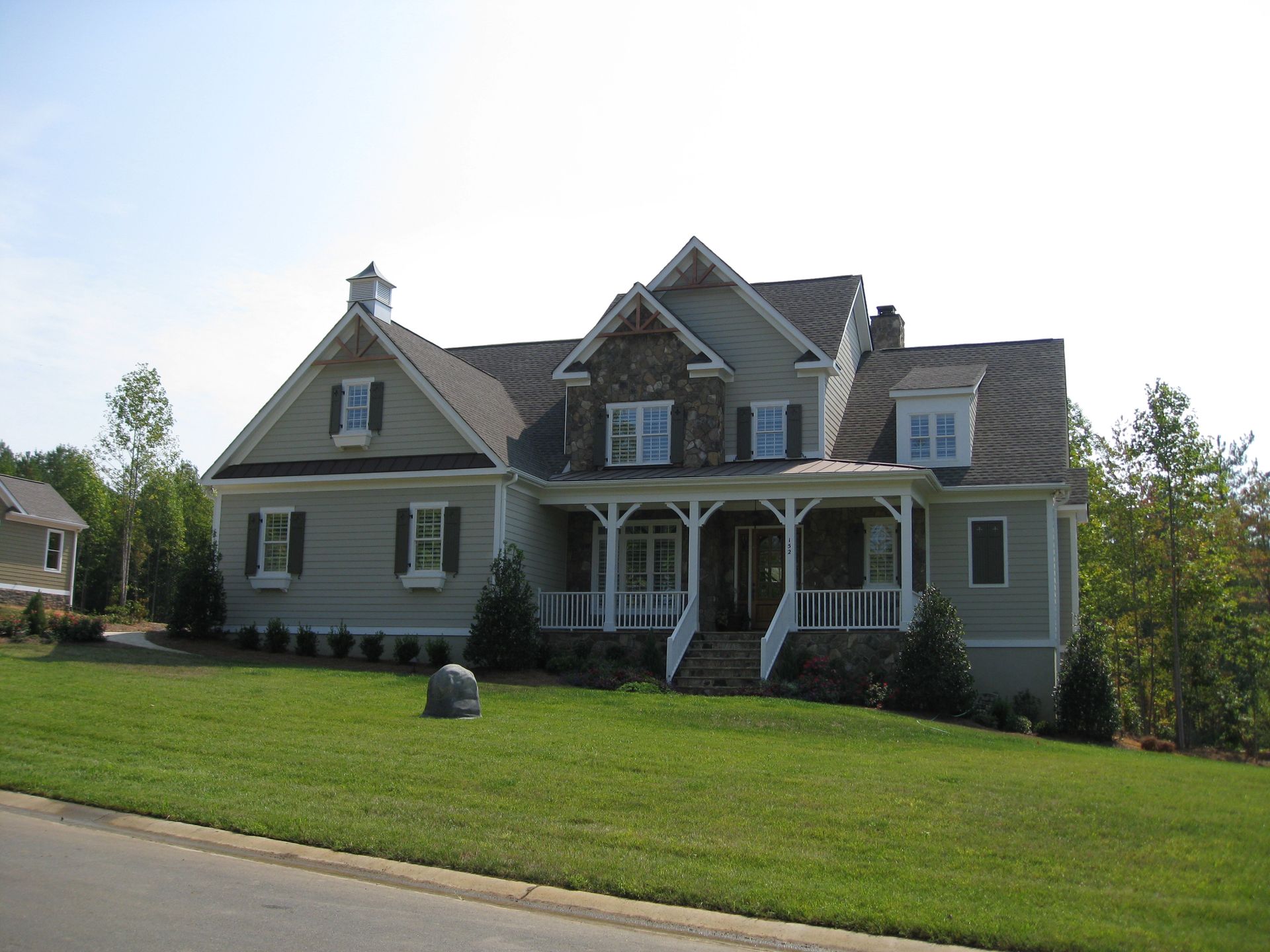 Large gray suburban house with a front porch and green lawn under a clear sky