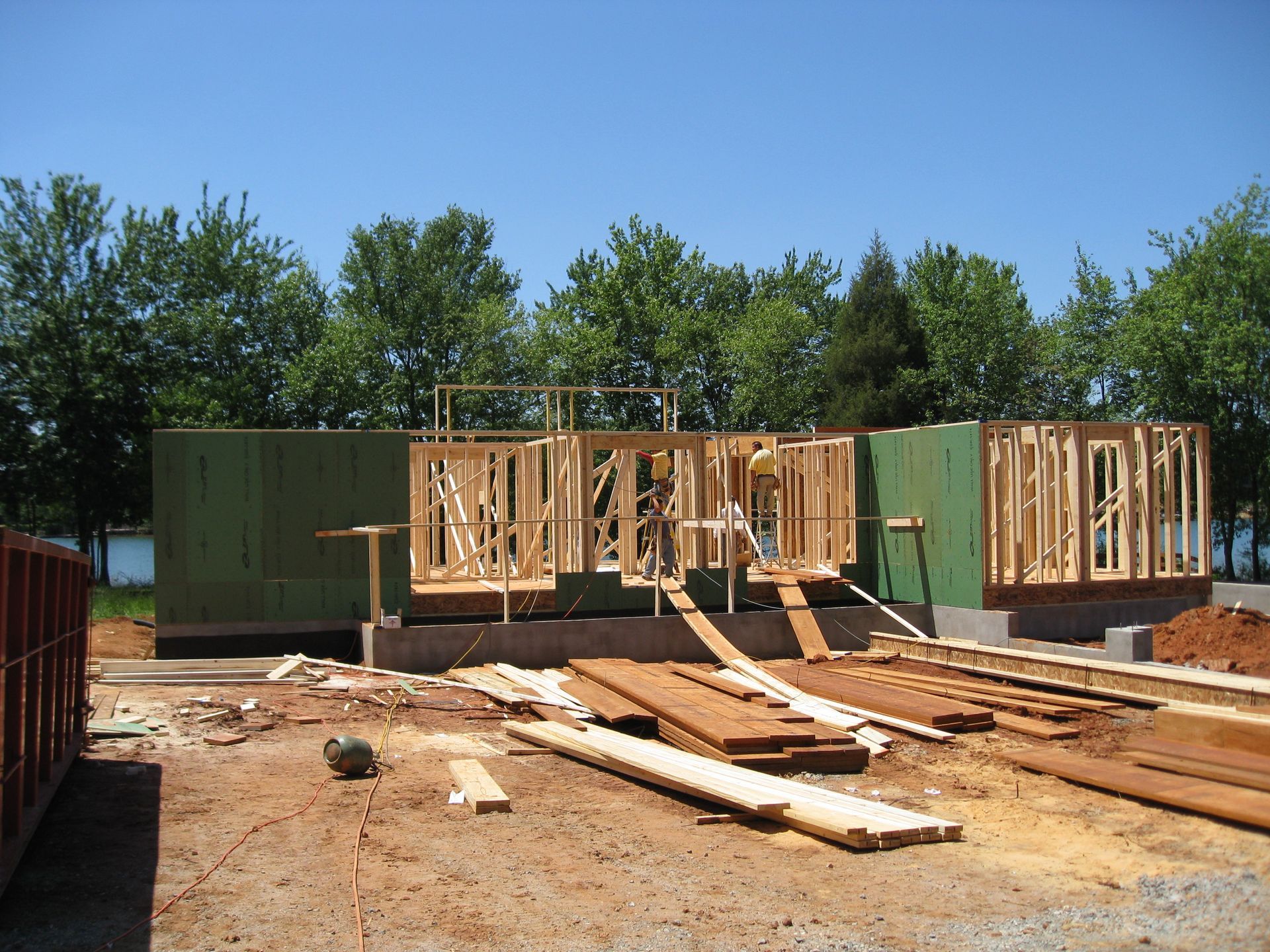 Partially built house with wooden framing and green walls at a construction site under a clear blue sky