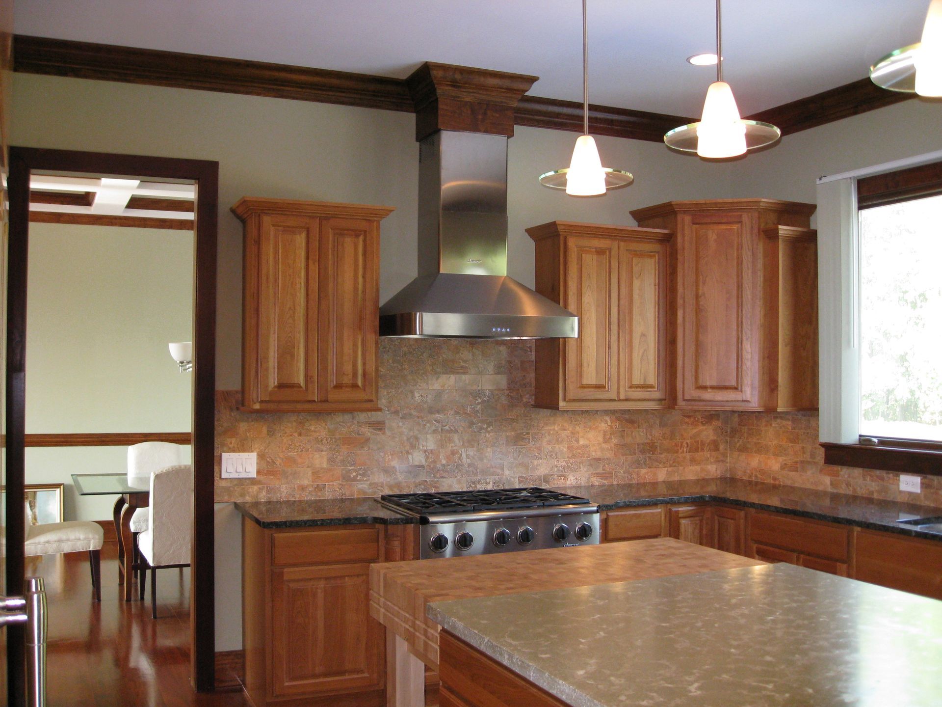 Modern kitchen with wooden cabinets, stainless range hood, granite island, and pendant lights