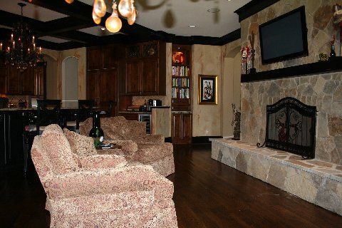 Cozy living room with patterned armchairs, kitchen cabinets, and a stone fireplace with a wall-mounted TV