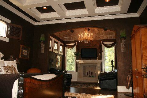 Cozy living room with dark walls, fireplace, chandelier, leather chairs, and a ceiling-mounted TV