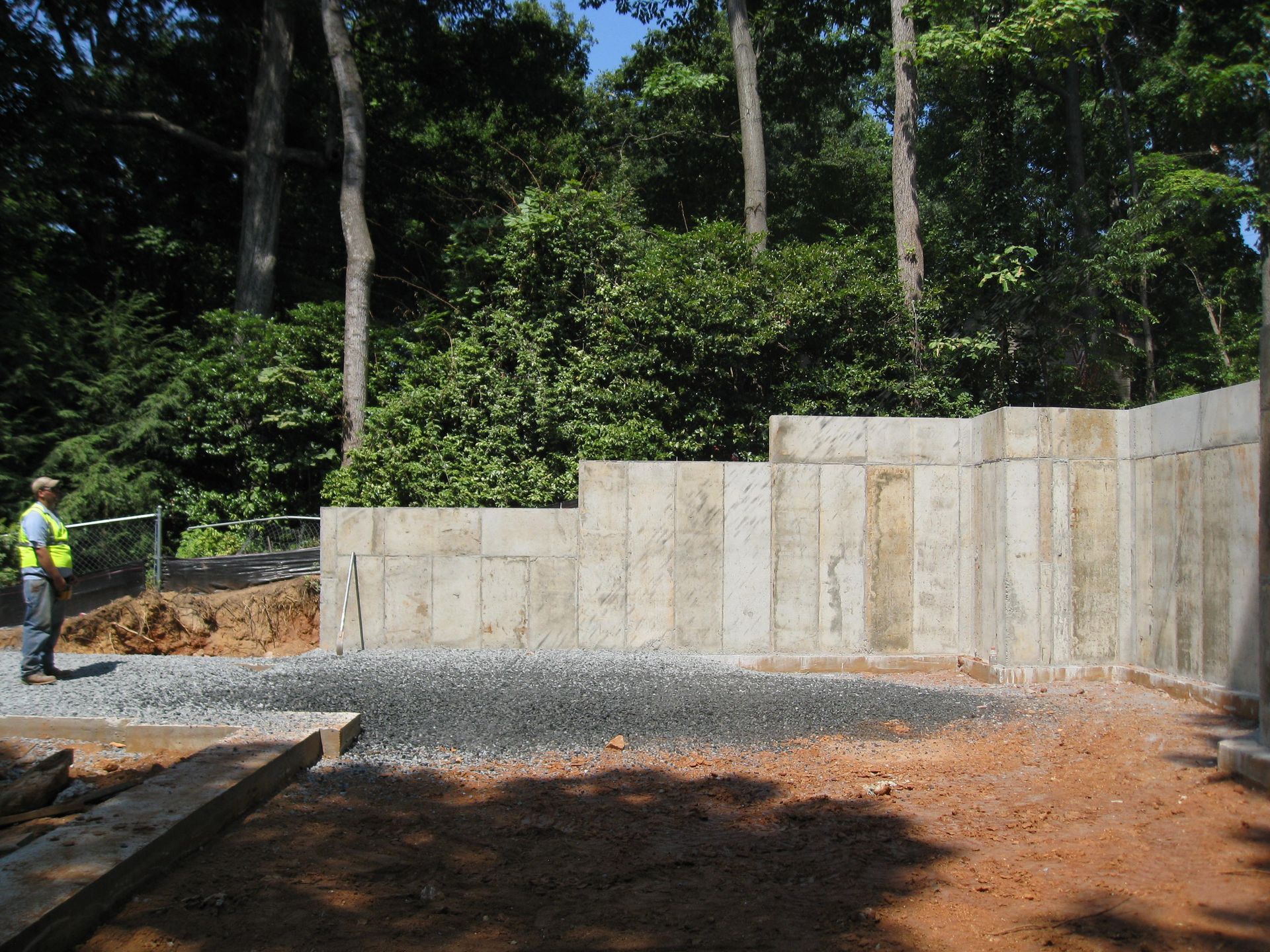 Construction worker beside concrete retaining wall in a wooded outdoor site