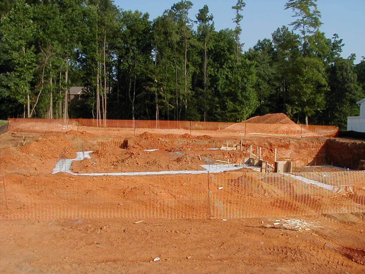 Excavated construction site with orange clay pit and trees in the background