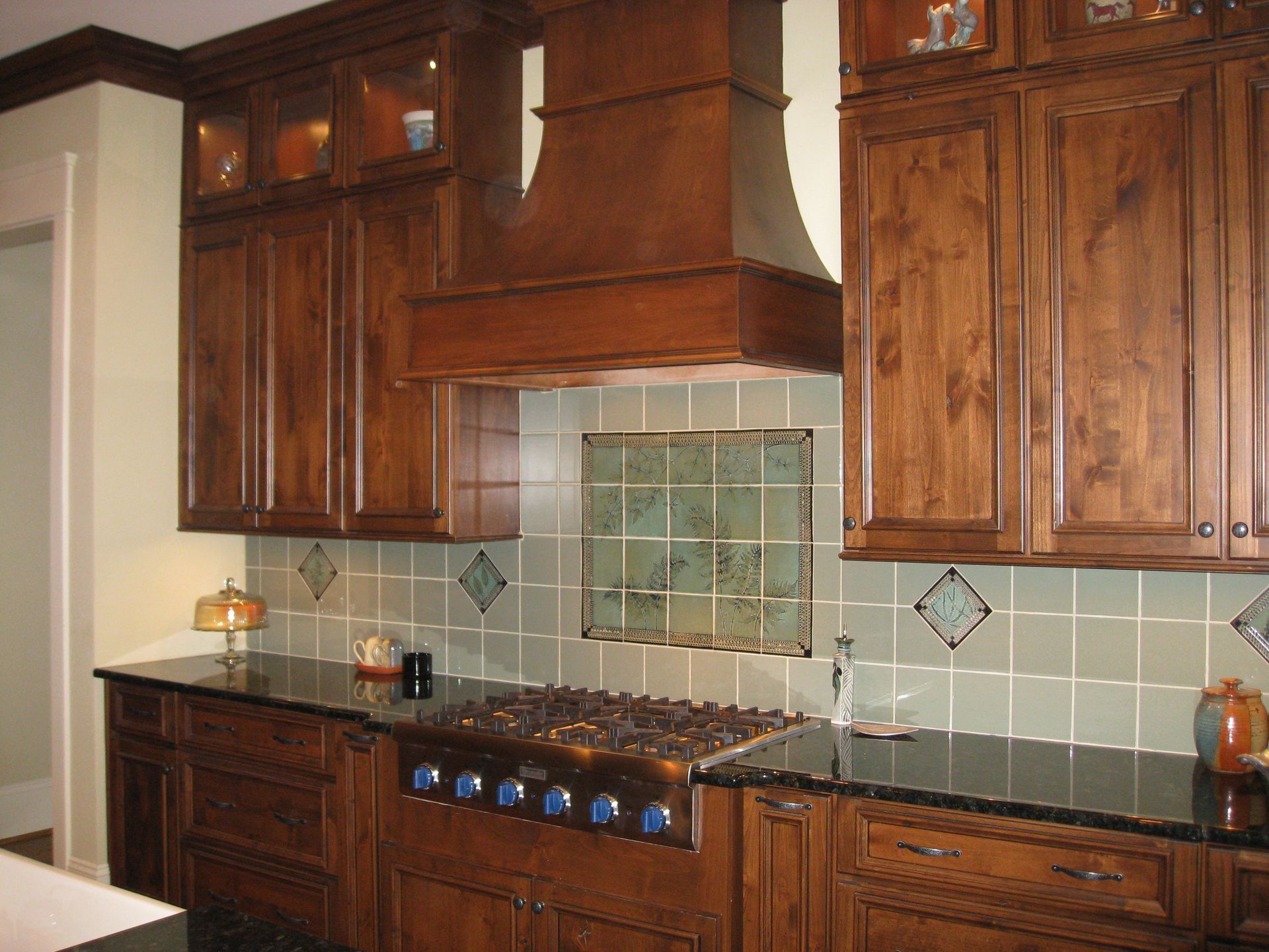 Modern kitchen with dark wood cabinets, green tile backsplash, and a stainless range hood