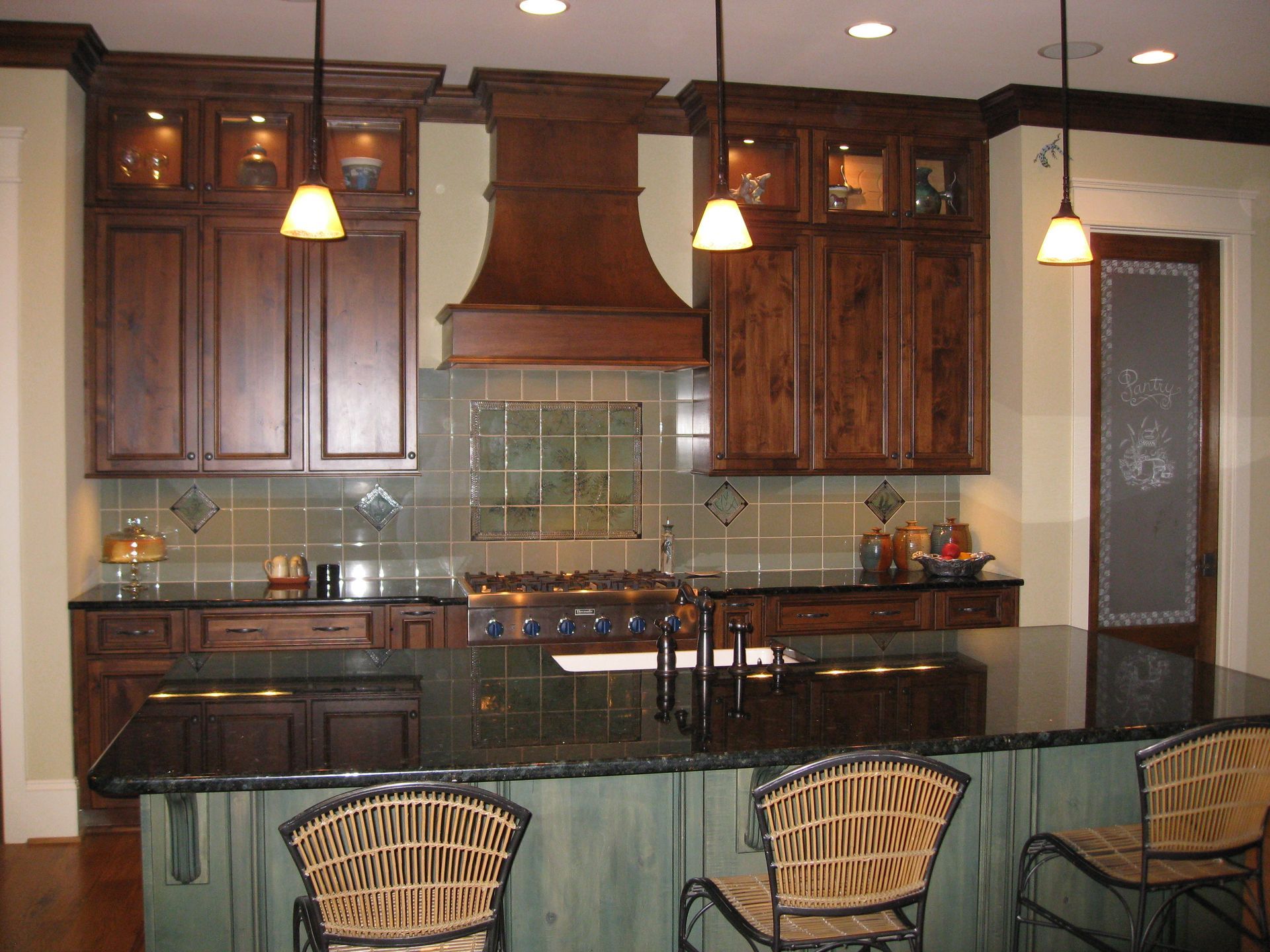 Modern kitchen with dark wood cabinets, black countertops, pendant lights, and two wicker stools at the island