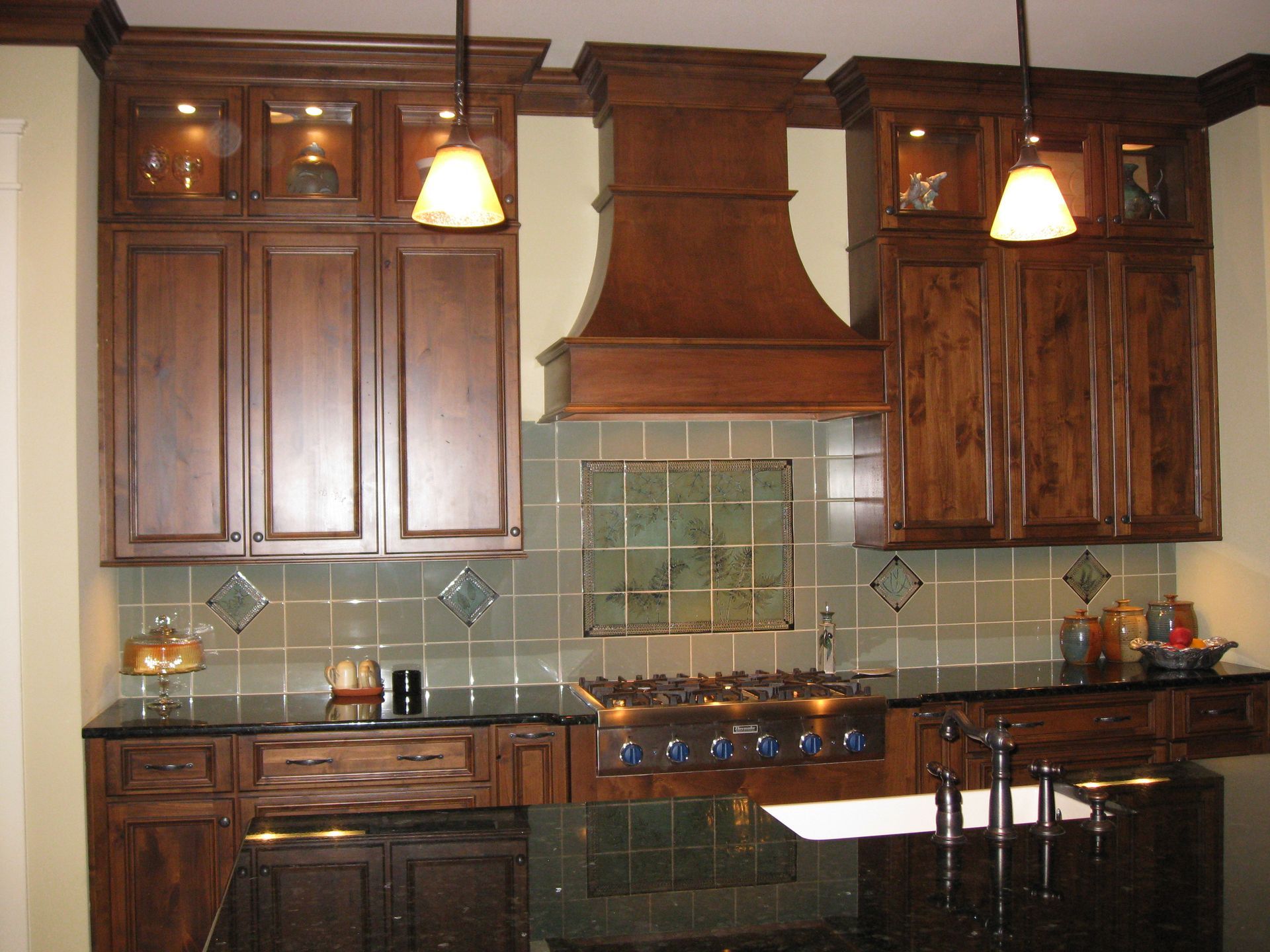 Wooden kitchen with green tile backsplash, copper hood, and hanging pendant lights