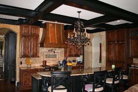 Elegant kitchen with dark wood cabinets, black island, chandelier, and coffered ceiling