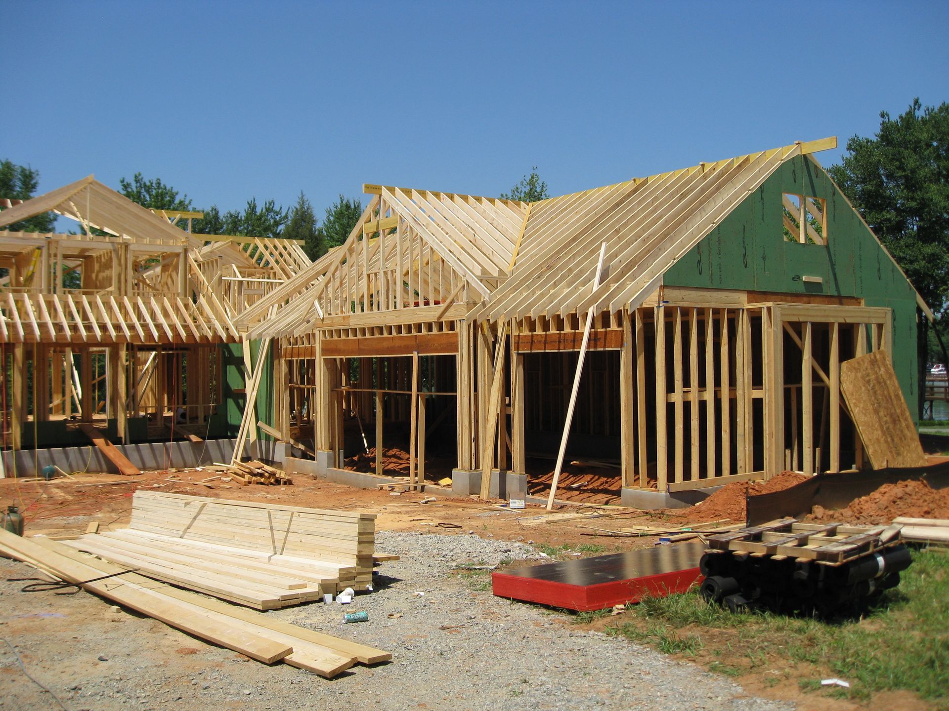 Partially built house with wooden framing and a green exterior under construction on a dirt lot