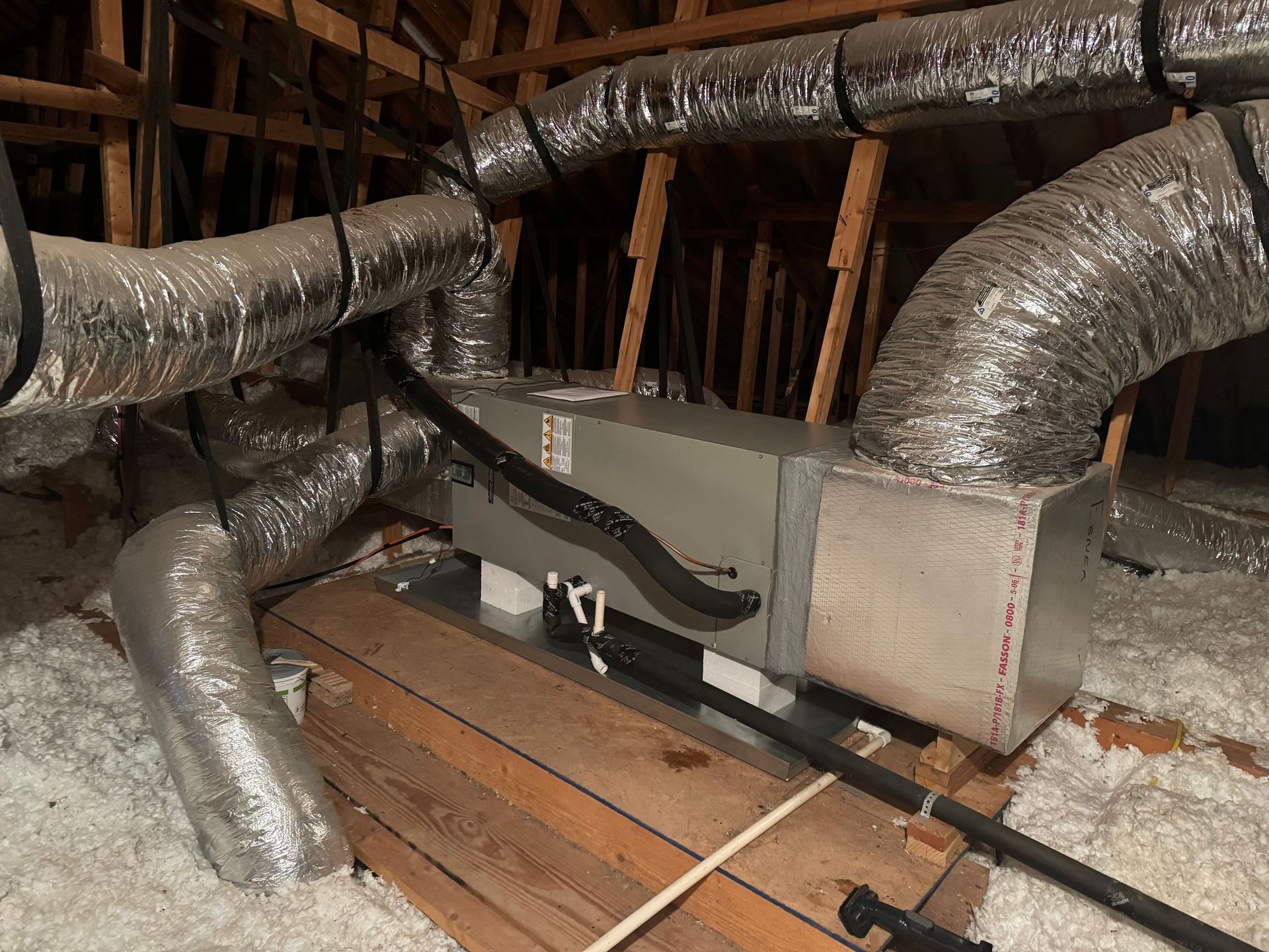 HVAC system in an attic. Metal ducts and unit on wooden supports, insulation on floor.