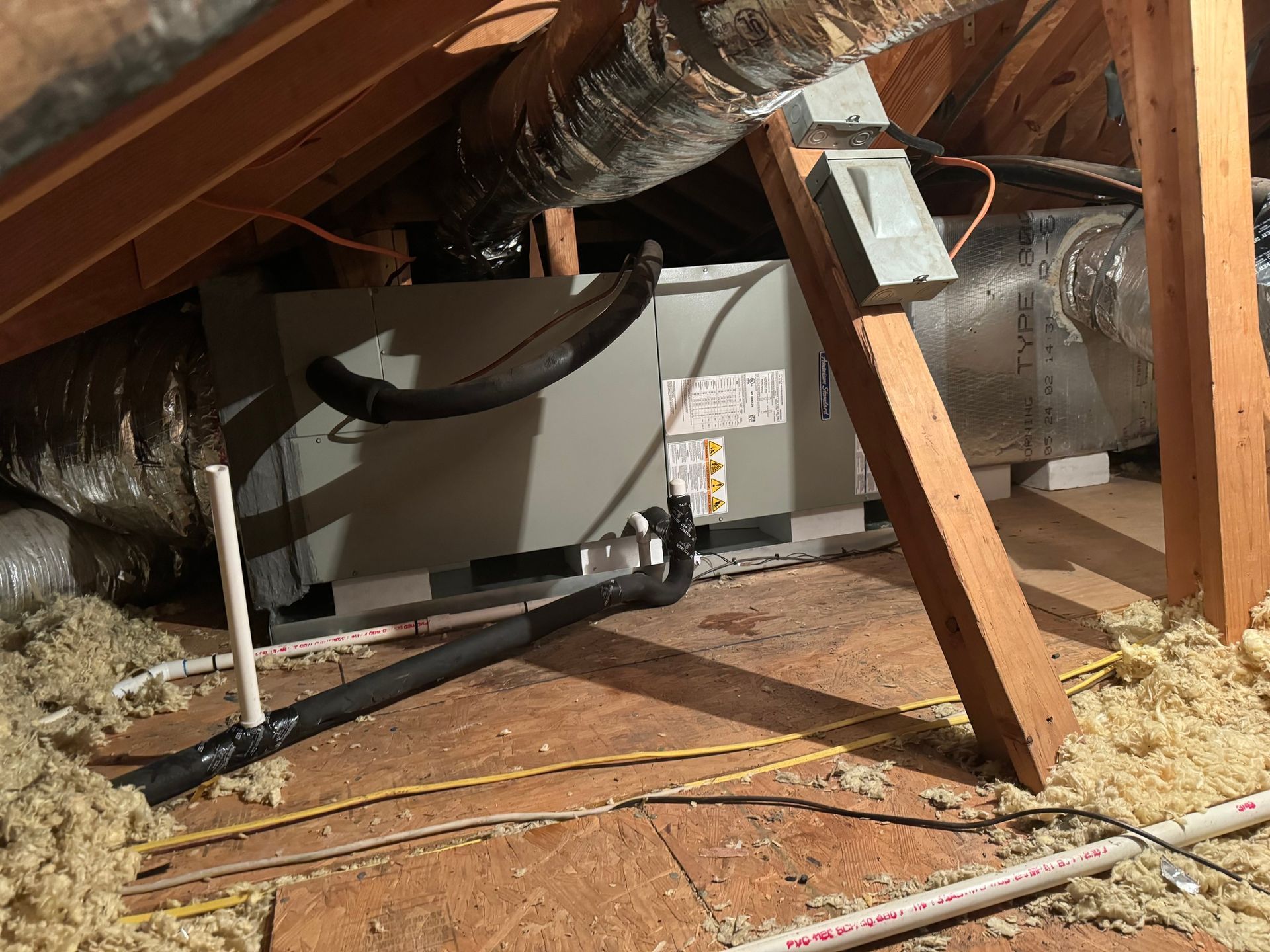 HVAC unit in an attic with ductwork, electrical components, and insulation. Wooden supports are present.