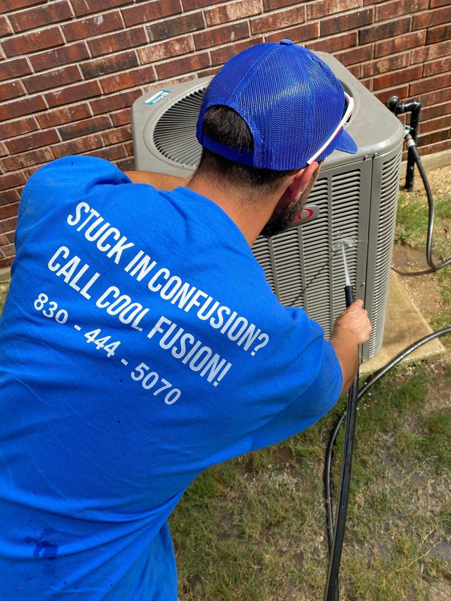 Man in blue shirt working on AC unit. Shirt text: 