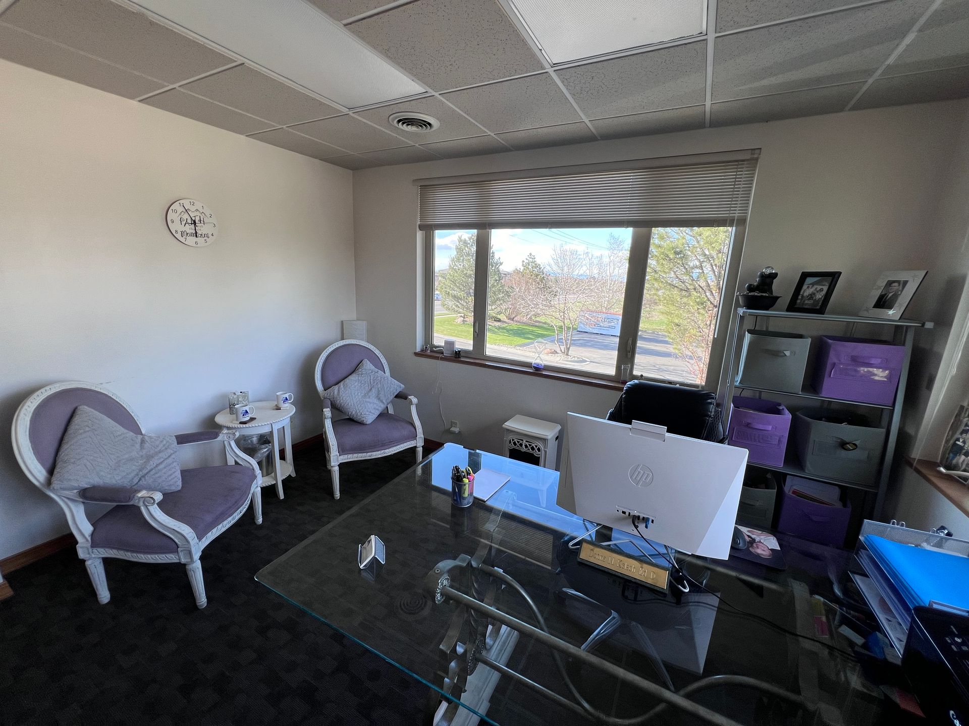 A room with a desk , chairs , a computer and a window.