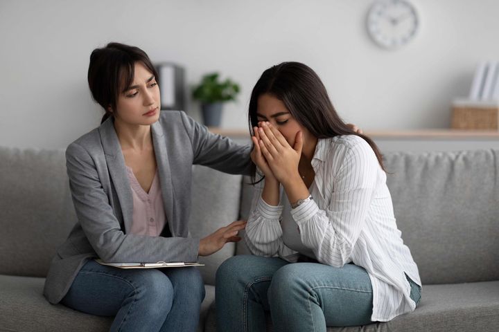 A woman is comforting a woman who is crying while sitting on a couch