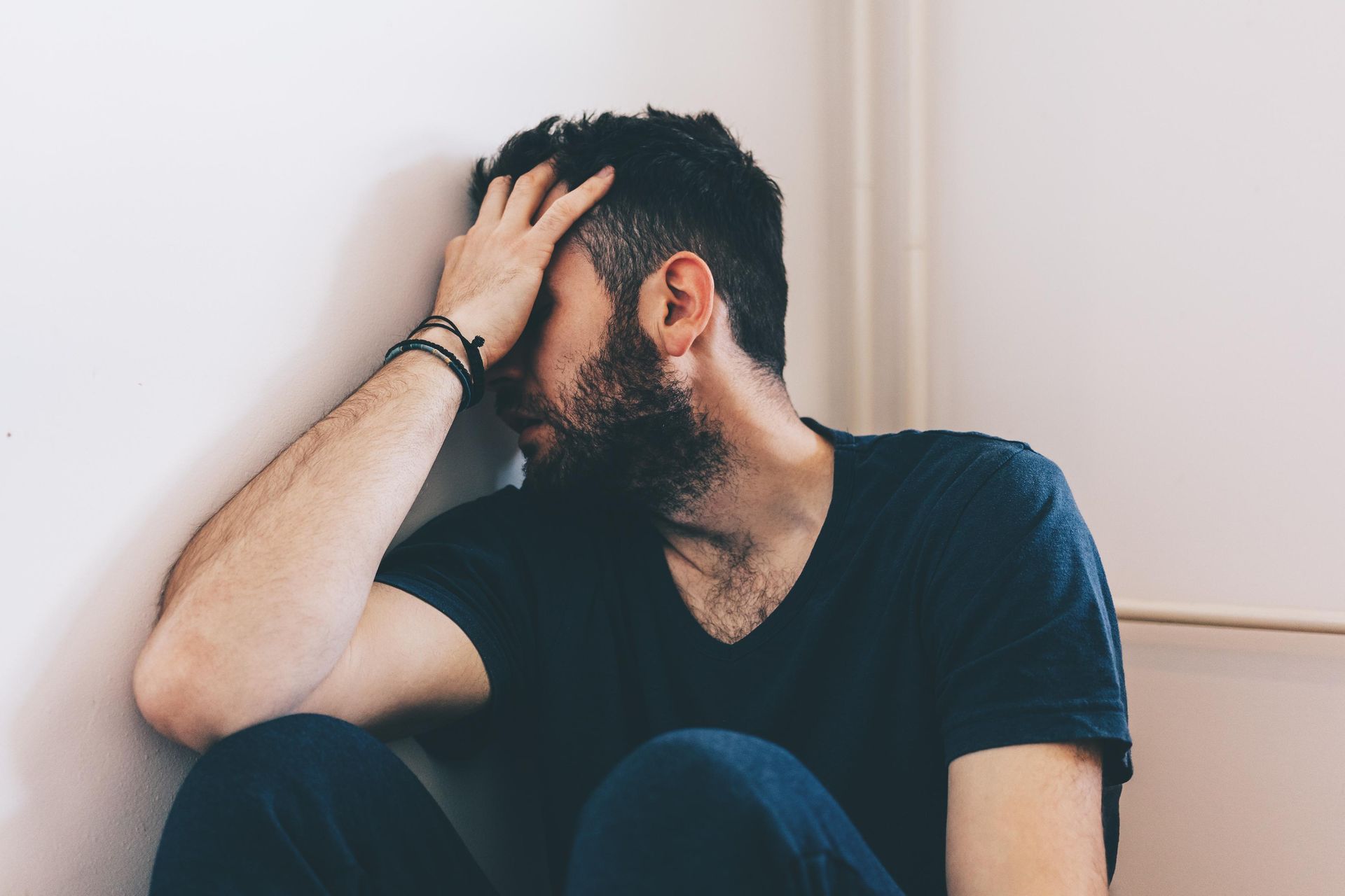 A man with a beard is sitting on the floor with his head against a wall