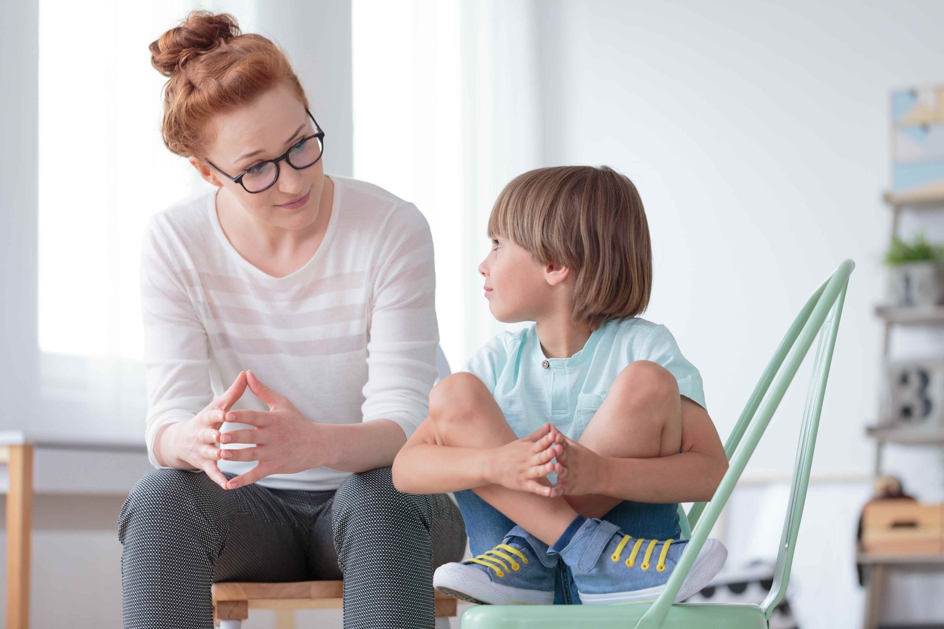 A woman is sitting on a chair talking to a young boy