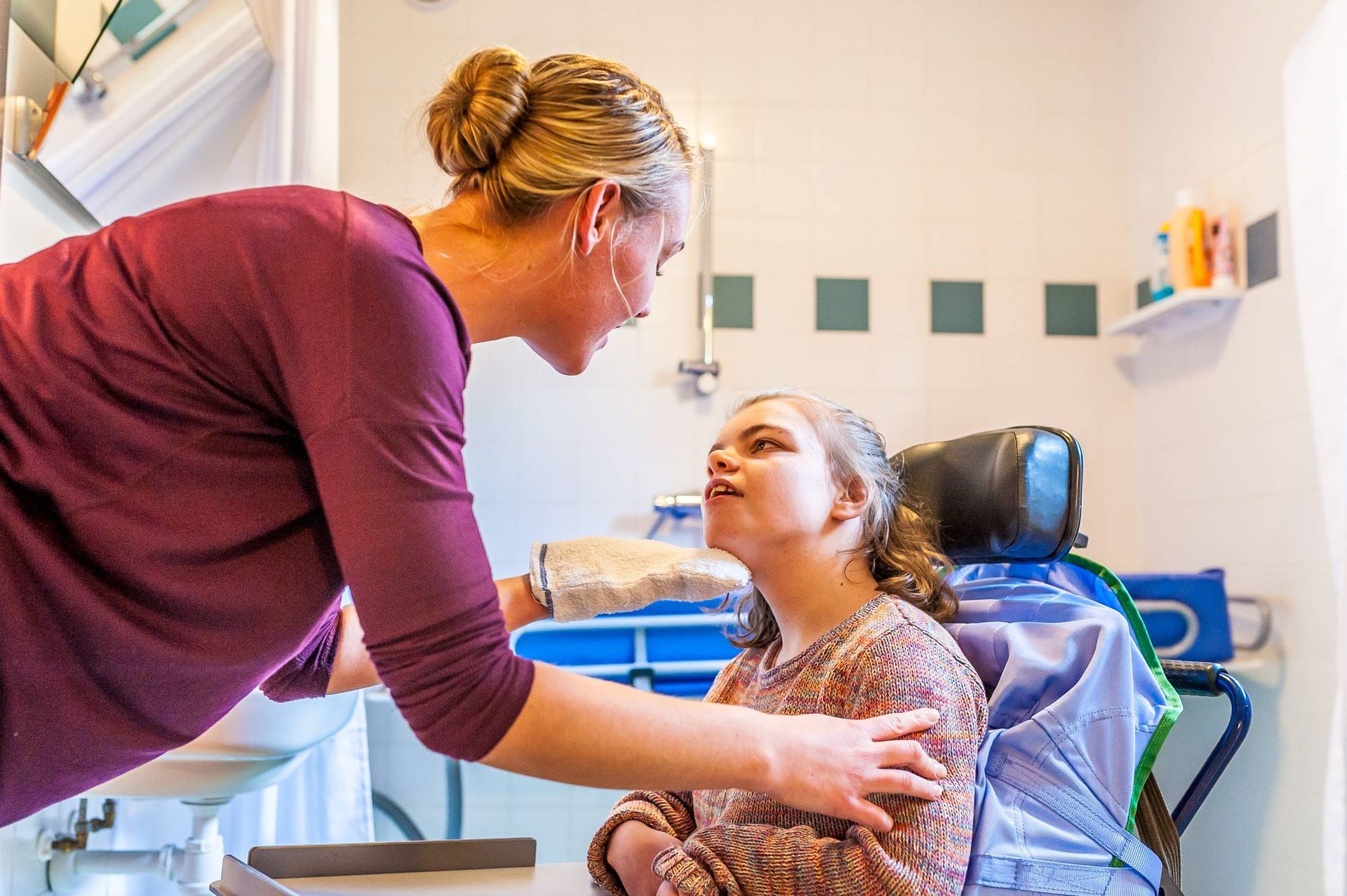 A woman is feeding a child in a wheelchair in a bathroom