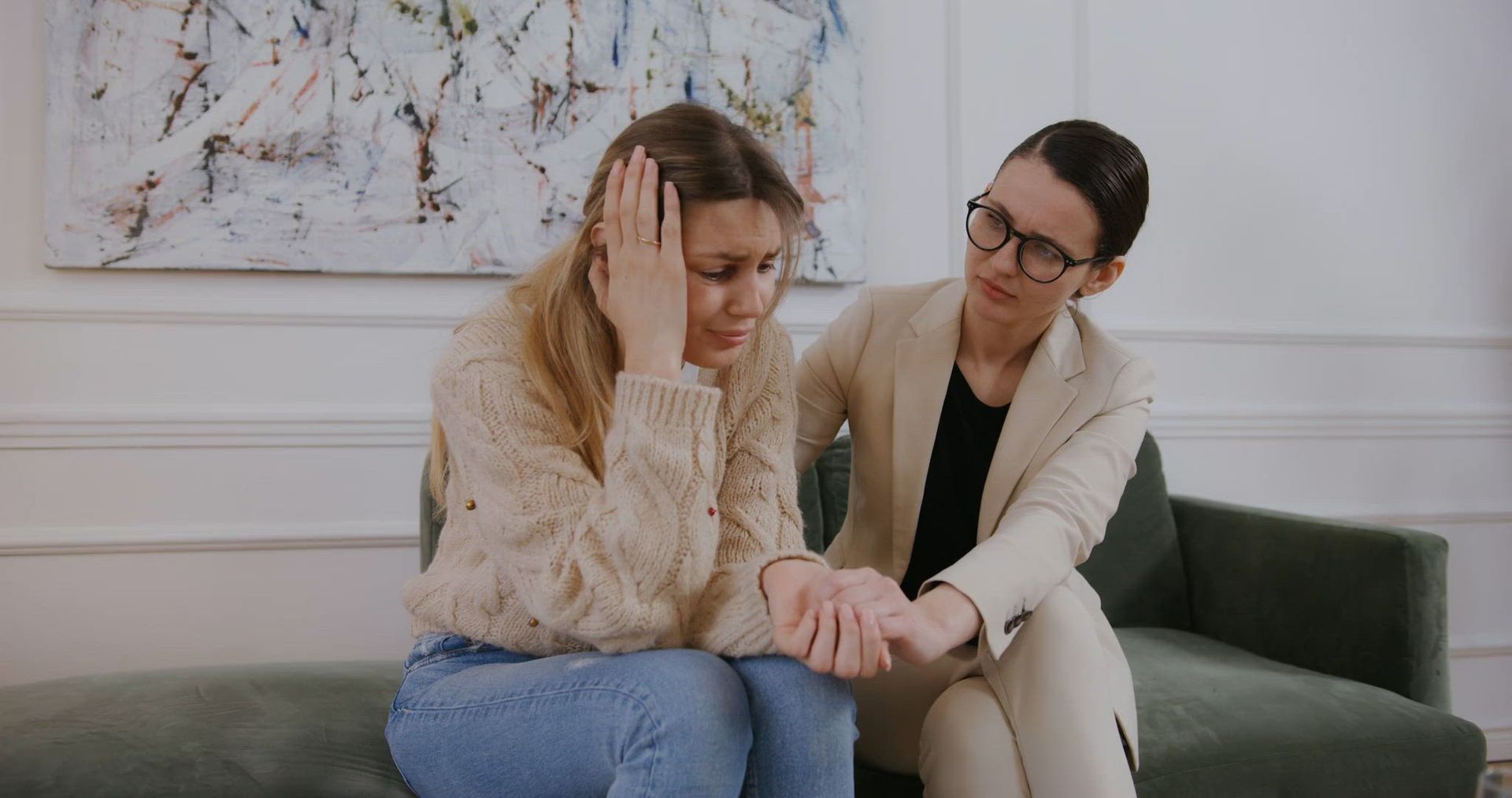 A woman is comforting another woman who is sitting on a couch.