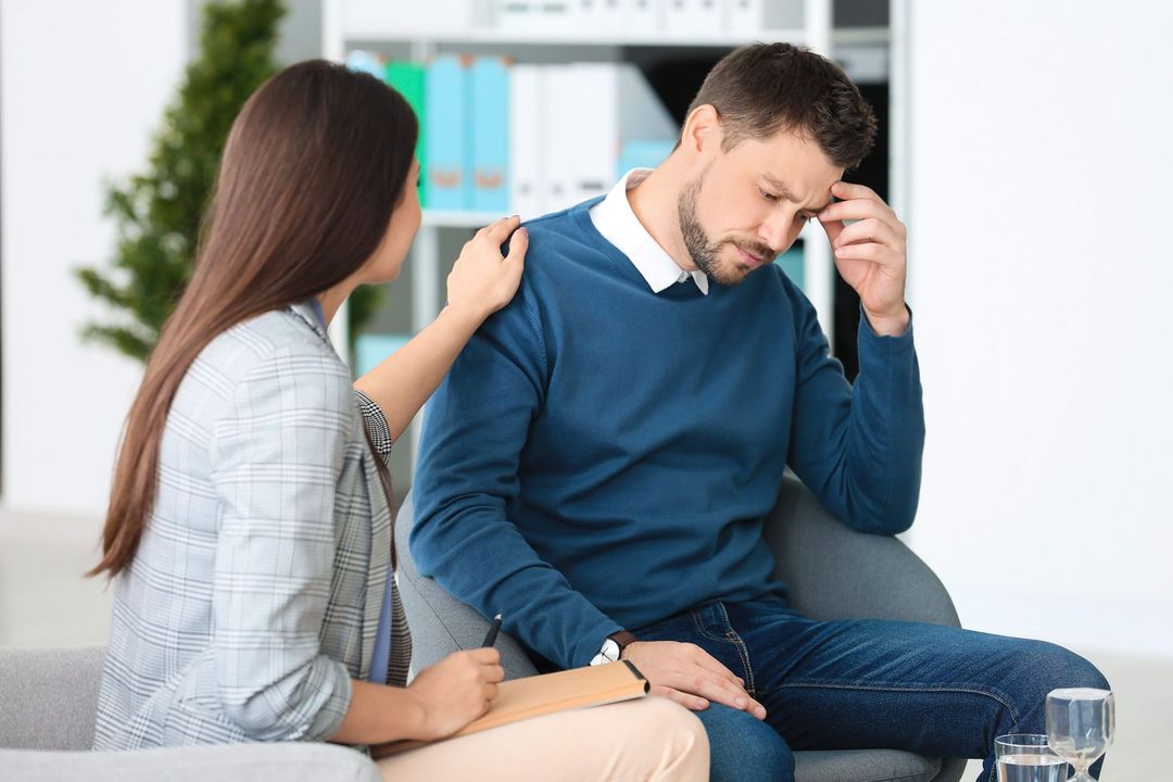 A woman is comforting a man who is sitting on a couch