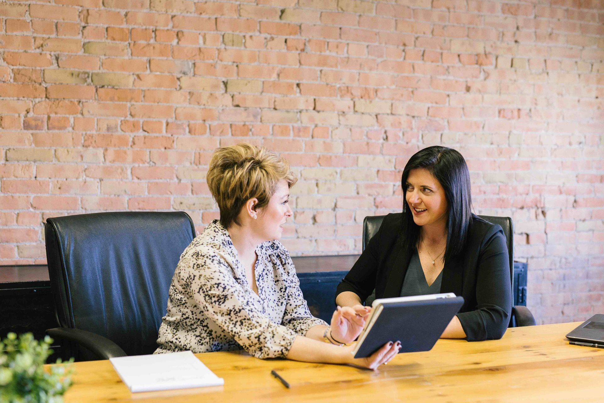 Two women are sitting at a table looking at a tablet.