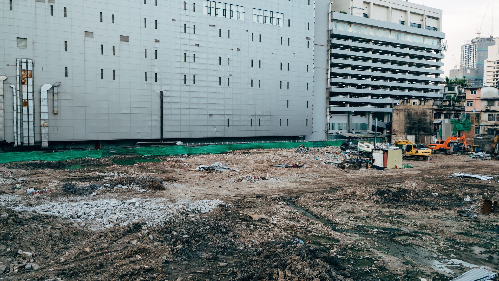 Construction site with debris and heavy machinery near a large, white building.