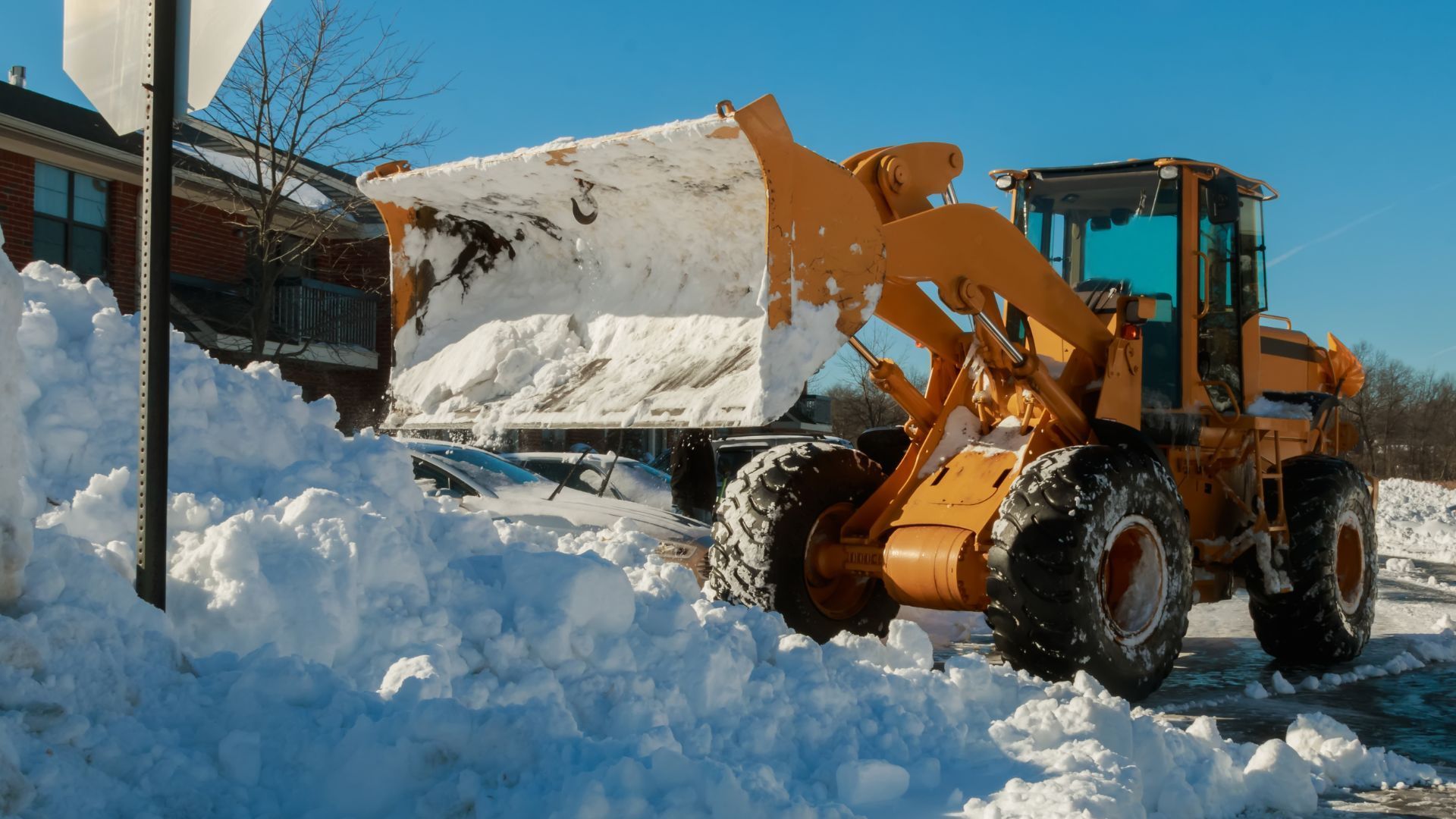 Yellow snowplow clearing snow on a sunny day.